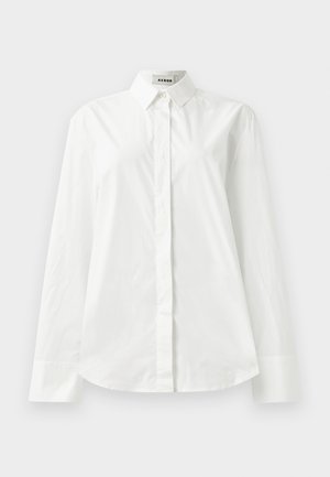 White cotton long-sleeve shirt with a pointed collar, button-front closure, and rounded hem. Smooth texture, regular fit, and no patterns.