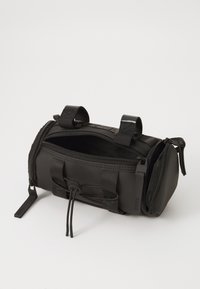 Borsa cilindrica nera compatta con due compartimenti con zip, spallacci regolabili e corda elastica su una superficie bianca.