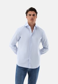 Helles blaues Langarm-Hemd mit klassischem Kragen, glatter Textur und weißen Knöpfen, kombiniert mit dunkelblauen Jeans.