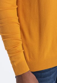 Yellow knit sweater with long sleeves, featuring a ribbed texture and cuffs. The fabric is smooth, and the design is fitted around the waist.