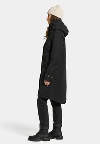 Zwarte waterdichte jas met een capuchon, met een rechte snit, knoopaccenten en zijzakken, gecombineerd met zwarte jeans en veterschoenen.