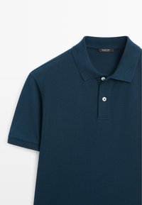 Marineblaues Kurzarm-Poloshirt mit zwei weißen Knöpfen, klassischem Kragen und subtiler Struktur, dargestellt auf weißem Hintergrund.