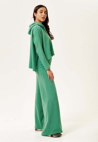 Green hoodie with a relaxed fit and long sleeves, paired with matching wide-leg pants, made of soft, textured fabric.