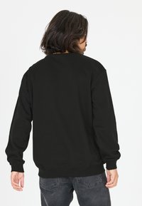 Musta huppari pitkillä hihoilla, pyöreällä kaula-aukoilla, ribaatit hihansuut ja helma. Kangas näyttää pehmeältä, siinä on tasainen pinta, eikä kuvioita tai logoja ole näkyvissä.