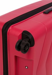 Tvrdý kufr v jasně růžové barvě s texturovaným povrchem, s černým kolečkem a zipem, a s zanořenou rukojetí blízko vrchu.