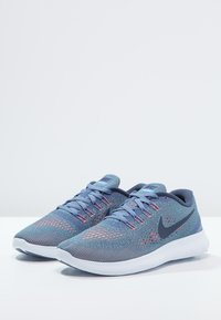 Modré pletené běžecké boty s texturovaným povrchem, lehkou podešví, bílou podrážkou a kontrastním tmavě modrým logem Nike na boku.