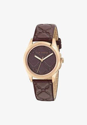 Bruine leren strap horloge met een ronde rosegouden kast. Geverfde donkere bruin wijzerplaat met gouden wijzers en gegraveerd logo. Decoratieve accenten zichtbaar.