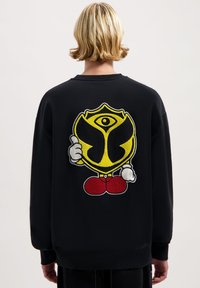 Zwarte sweatshirt met een textuur, kleurrijk geborduurd ontwerp waarop een personage met een gele embleem op de rug staat.