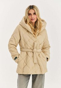 Béžová prošívaná bunda s velkou kapucí, stahovacími páskem v pase a diagonálním prošíváním. Dvě boční kapsy a texturovaný povrch.