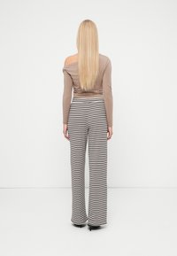 Long-sleeve, taupe top with off-shoulder design paired with high-waisted, black-and-white striped wide-leg pants. Smooth fabric, elegant cut.