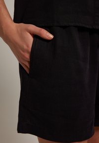 Černé lněné šortky s bočními kapsami, uvolněným střihem a hladkou texturou s pečlivě dokončenými lemy. Ručně umístěné v kapse.