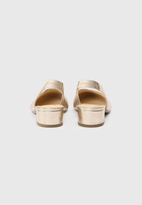 Guldmetallic slip-on sko med lav blokhæl, rundet tå og glat tekstur. Har en bagudvendt design og diskrete syningsdetaljer.