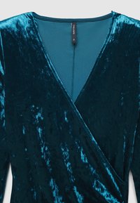 Haut en velours teal avec un décolleté en V profond, un tissu texturé et une doublure lisse. L'étiquette indique le nom de la marque "Calliope" et la taille "S."