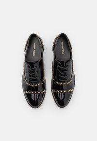 Svarta lackskor med snörning, prydda med nitar och en slät finish. Platta sulor och rundad tåform.