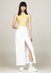 Larga falda de mezclilla blanca con una abertura frontal, combinada con una camiseta ajustada amarilla y zapatillas blancas. Textura suave y diseño casual.