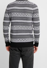Czarno-biały sweter na drutach z geometrycznymi wzorami, prążkowanymi mankietami i krawędzią. Wzór obejmuje naprzemienne pasy z motywami i paskami.