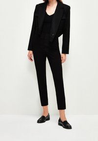 Černý zkrácený blejzr s klopami, doplněný o přiléhavý černý top a zúžené černé kalhoty. Outfit doplňují černé loafers.