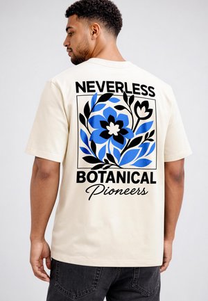 Man wearing a cream T-shirt with blue and black floral design and text "Neverless Botanical Pioneers" on the back.