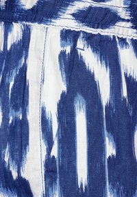 Bomulls tyg med ett blått och vitt ikat-mönster, med en texturerad väv och rynkade detaljer längs den övre kanten.