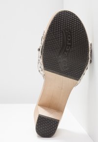 Semelle d'une chaussure à talon en bois avec caoutchouc noir texturé au talon et à l’orteil, affichant le nom de la marque "SOELETTOX" embossé sur la semelle.