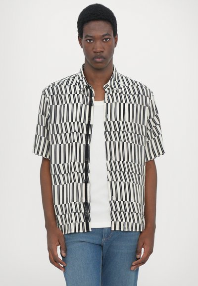 Short-sleeve shirt in a black and white striped pattern, featuring textured fabric and button closure, worn over a white tank top.