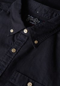 Navyblauwe shirt met een button-down kraag, voorzien van vier lichtgekleurde knopen, een borstzak en subtiele stikseldetails.