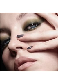 Nahaufnahme eines Gesichts mit olivgrünem Lidschatten, grauen, mandelförmigen Nägeln und sanften Lippen. Die Haut wirkt glatt mit definierten Augenbrauen und Wimpern.