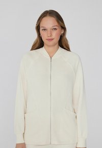 Krémová mikina na zip s raglánovými rukávy, předn�ími kapsami a hladkou strukturou. Minimalistický design a měkká tkanina v světlé barvě.