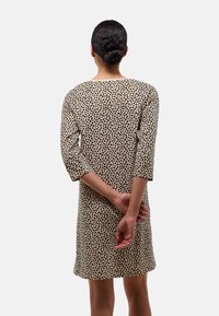 Robe beige à taches léopard noires, manches 3/4, encolure arrondie, longueur mi-cuisse, tissu doux, design simple, vue de dos.