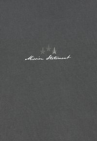 Γκρι ύφασμα με λευκό κείμενο σε γραφή χειρόγραφου τύπου "Δήλωση Αποστολής" κάτω από τρία ξεθωριασμένα αστέρια τοποθετημένα σε οριζόντια σειρά.