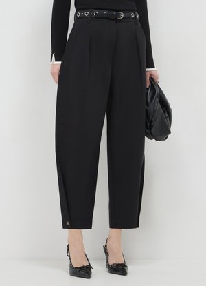 Pantalon noir à jambes larges avec plis, taille ajustée avec éléments argentés et détail bouton à l'ourlet, porté avec des chaussures noires à talons.