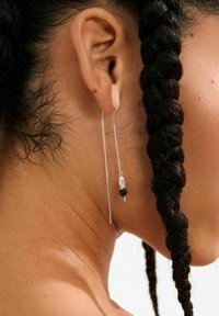 Silberne, hängende Ohrringe bestehen aus einer feinen Kette mit einer schwarzen Perle, einer klaren Perle und einem kleinen lila Akzent, die einen geschichteten Effekt erzeugen.