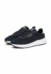 Baskets en mesh noir avec semelle blanche, design à lacets, tige texturée et branding subtil sur le côté et la languette. Construction légère.