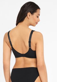 Svart bh med justerbara remmar, mjuk textur och enkel design. Har en hak-och-ögla stängning på baksidan.