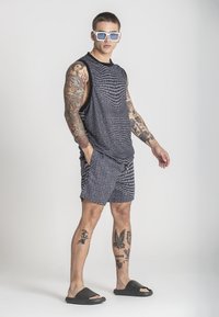 Majica bez rukava s crno-bijelim uzorkom i kratke hlače, s opuštenim krojem. Tamne sandale i naočale s bijelim okvirom. Glatka, lagana tkanina.