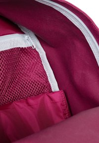 Fuchsia ryggsäckens insida med en vit dragkedja, nätficka och slät tygstruktur. Olika fack synliga för organisering.