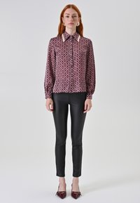 Blusa bordeaux a fantasia con colletto a punta e chiusura a bottoni, abbinata a pantaloni neri attillati e décolleté bordeaux a punta.