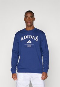 Blå bomuldssweatshirt med et stort "ADIDAS" logo, et lille grafisk motiv for "TENNIS CLUB" og lange ærmer med ribkant.