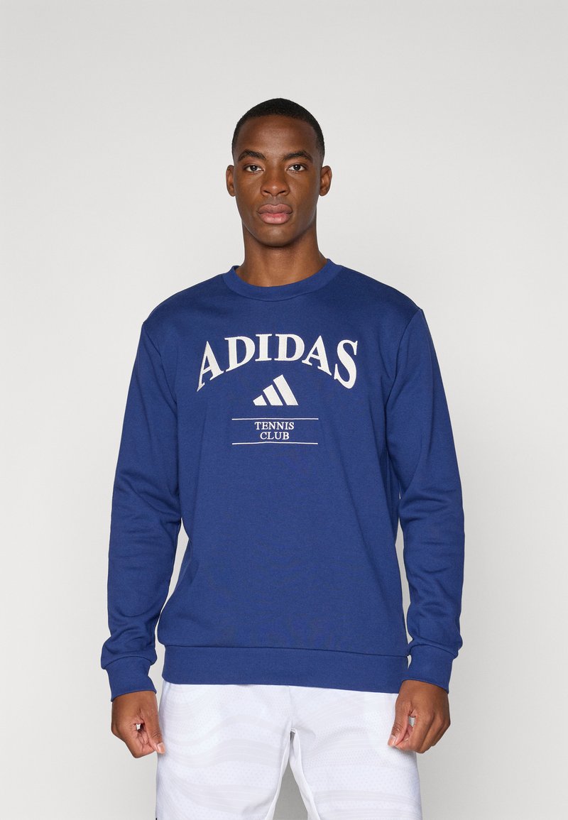 Μπλε φούτερ με μακριά μανίκια, στρογγυλή λαιμόκοψη και λευκό γραφικό "ADIDAS TENNIS CLUB". Κατασκευασμένο από λεία ύφανση, διαθέτει ριμπ τελειώματα στα μανίκια και στη μέση.