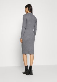 Grau geripptes Strickkleid mit langen Ärmeln, hohem Kragen und wadenlanger Länge. Kombiniert mit schwarzen Blockabsatz-Ankle Boots.