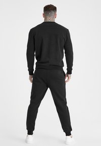 Conjunto de sudadera y pantalones jogger en negro, fabricado en una mezcla de algodón. Presenta puños y dobladillo acanalados, con una textura suave y un perfil ajustado.