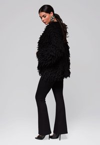 Svart, ruggig cardigan med texturerade, långa fibrer. Matchat med figurnära svarta utsvängda byxor och högklackade sandaler. Anmärkningsvärda överdimensionerade blommörhängen.