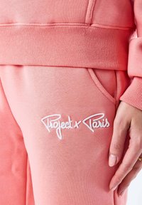 Lichtroze sweatshirt met ribgebreide manchetten en tailleband. Heeft een witte geborduurde logo "Project x Paris" op het linkse zakgebied.