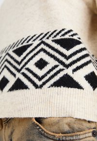 Gebreide trui met een geometrisch zwart en crèmekleurig patroon bij de halslijn, met een rib gebreide zoom en een zachte textuur. Gecombineerd met denim.