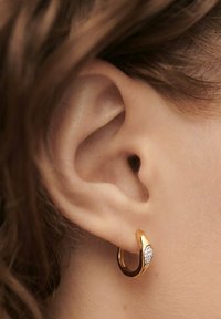 Guld hoop ørering med et buet design og en glat overflade, med et afsnit prydet med små klare ædelsten.