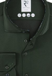 Donkergroene gebreide shirt met een kraag, knoopsluiting en een gestreepte binnenvoering. Het heeft een borstzak en textuurstof.