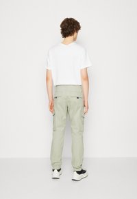 Ljusgröna cargobyxor med elastiska muddar, två sidofickor och två bakfickor. Matchas med en enkel vit t-shirt och svarta sneakers.