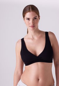 Sort ribstrikket bralette med v-halsdesign og brede stropper, der har en omslagsfrontstil, og som viser en glat tekstur og minimalt hardware.
