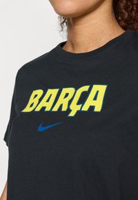 Μαύρο βαμβακερό μπλουζάκι με κίτρινο κείμενο "BARÇA" και μπλε λογότυπο Nike. Κοντά μανίκια και κλασικός σχεδιασμός με στρογγυλή λαιμόκοψη.
