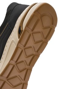 Zapatilla negra con un upper texturizado y una suela de goma beige que presenta un diseño de banda de rodadura para mayor agarre. Acabada con un pequeño detalle negro.